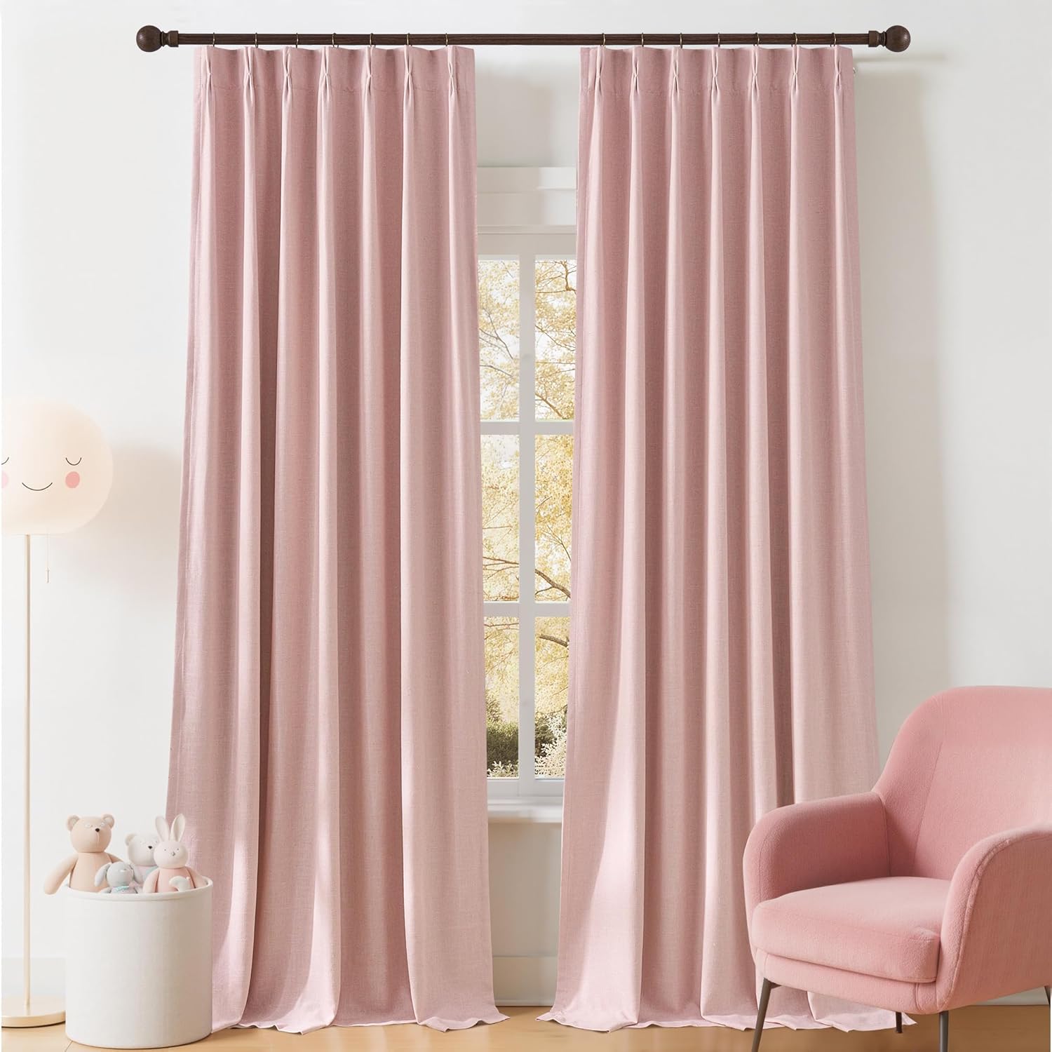 Two blush pink textured linen curtains with pinch pleats hanging on a window rod in a child's room.