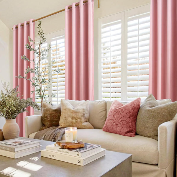 Soft blush pink grommet top window curtains hanging on a gold rod in a sunny living room.