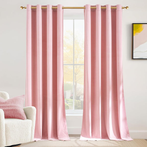 Soft blush pink velvet curtains with gold grommet tops hang on a gold rod by a bright window.