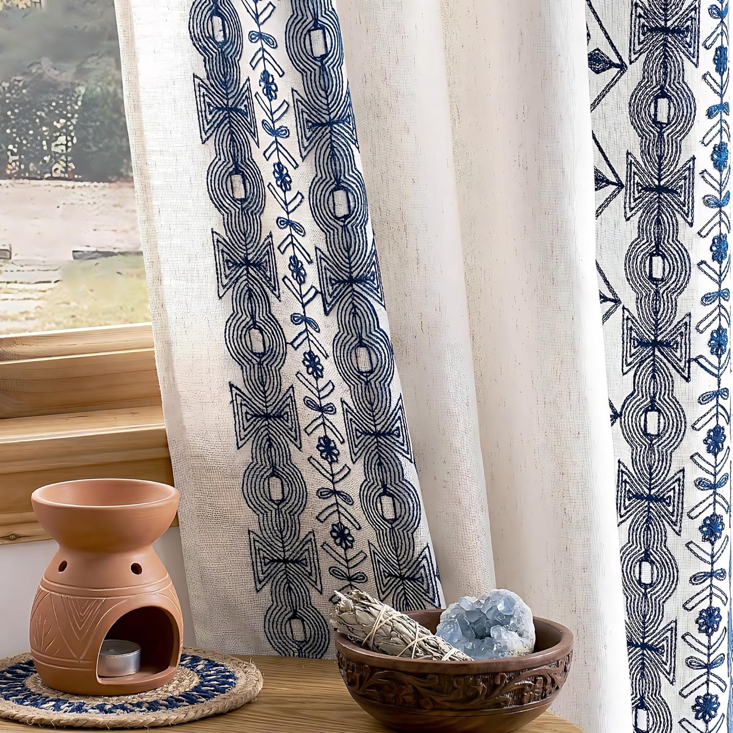 Off-white sheer curtains feature a vertical blue embroidered bohemian pattern with geometric and floral motifs.