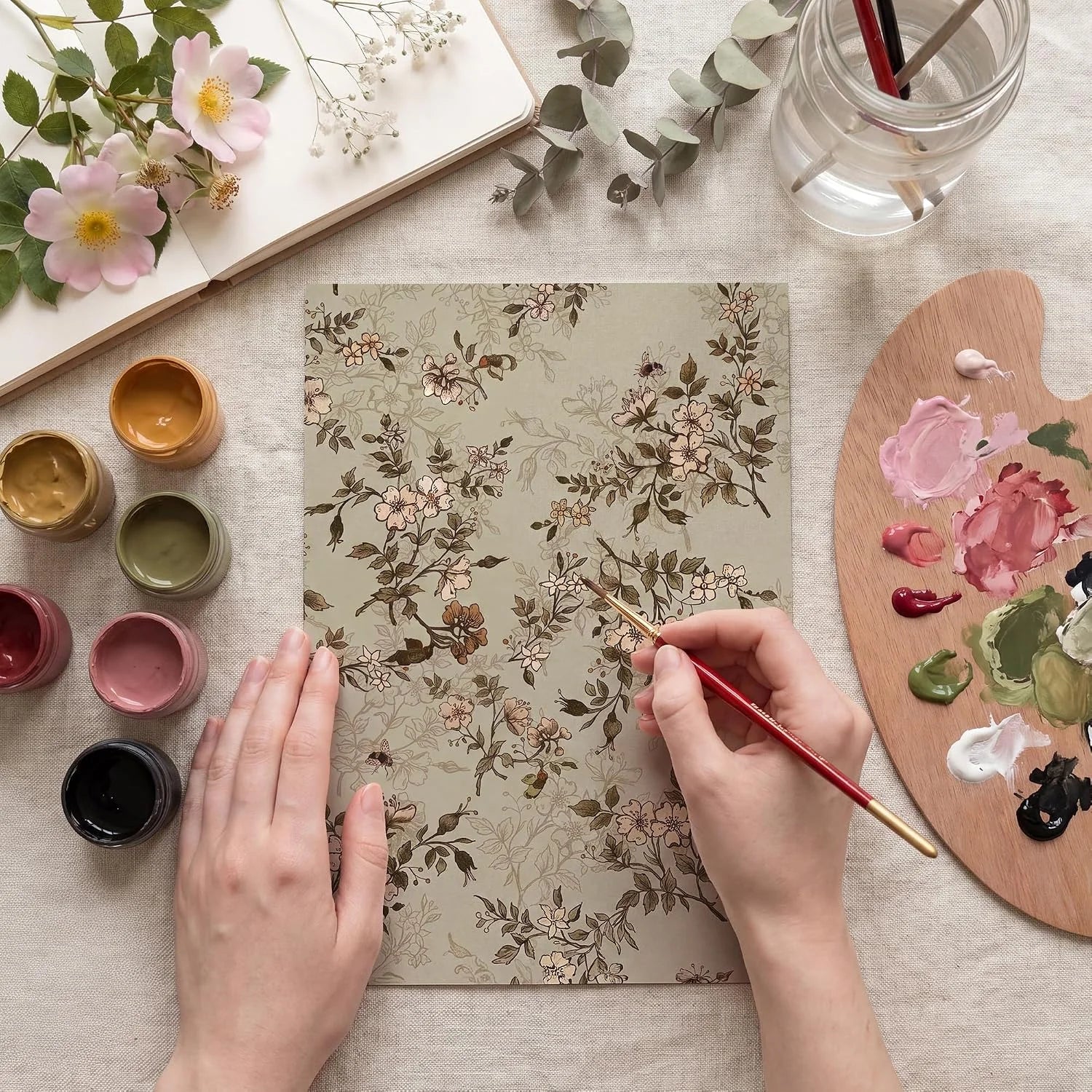Hands painting a delicate floral botanical pattern with gouache on paper
