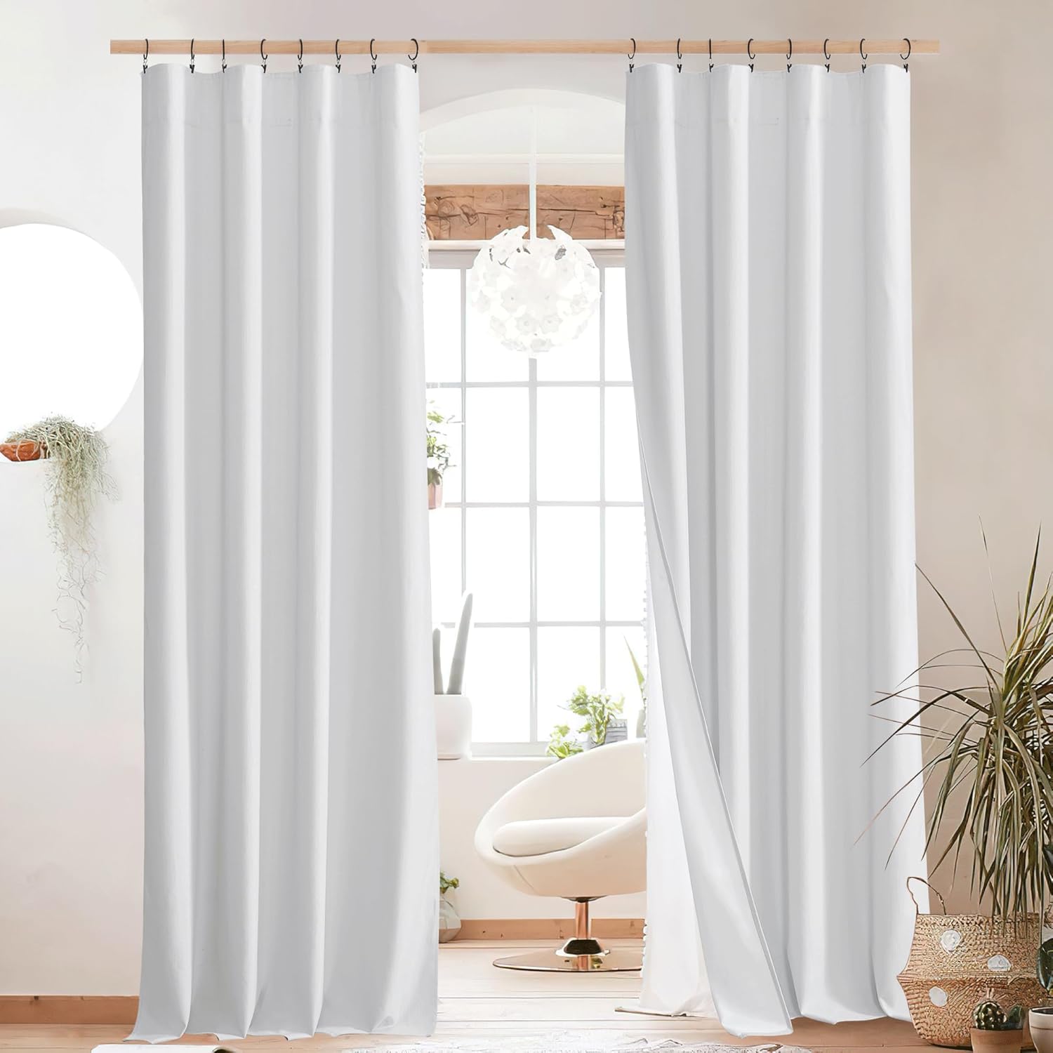 Bright white opaque panel curtains hanging on a wooden rod with black hooks in a modern living room.