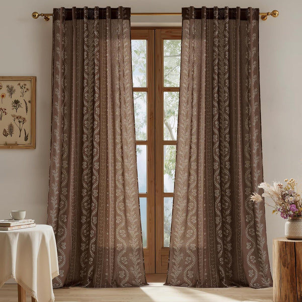 Dark brown grommet curtains with light floral vine embroidery. Hung over a wooden window, they filter natural light.