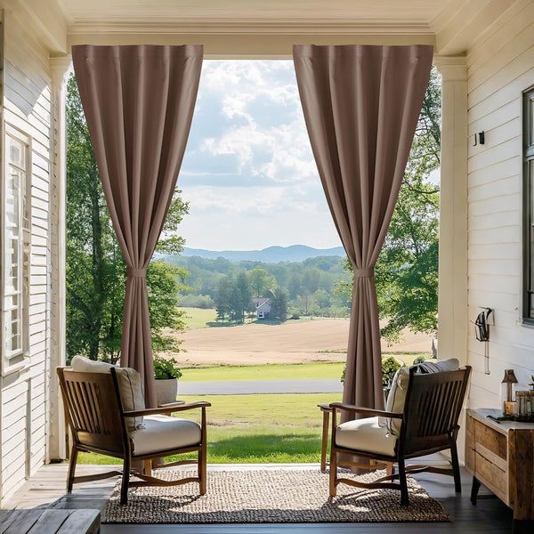 Pair of brown outdoor curtains tied back on a porch, framing a view of green fields and distant hills.