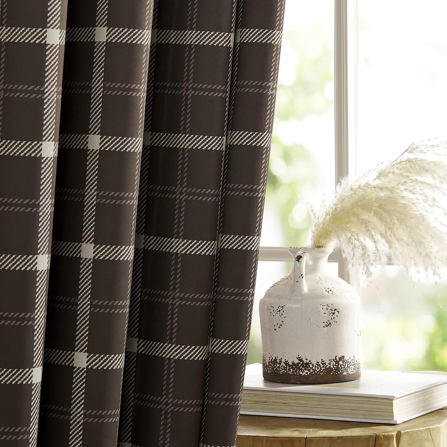 Brown plaid curtain panel beside a bright window with a rustic white ceramic vase