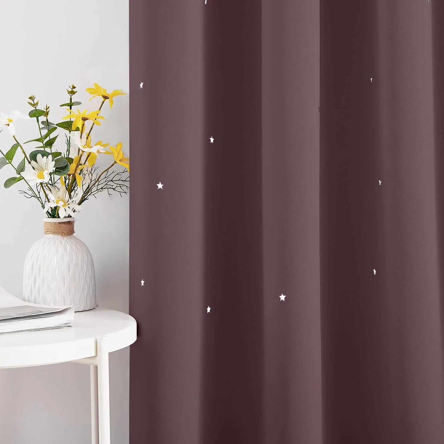Brown blackout curtain with small white star print beside a white side table and vase