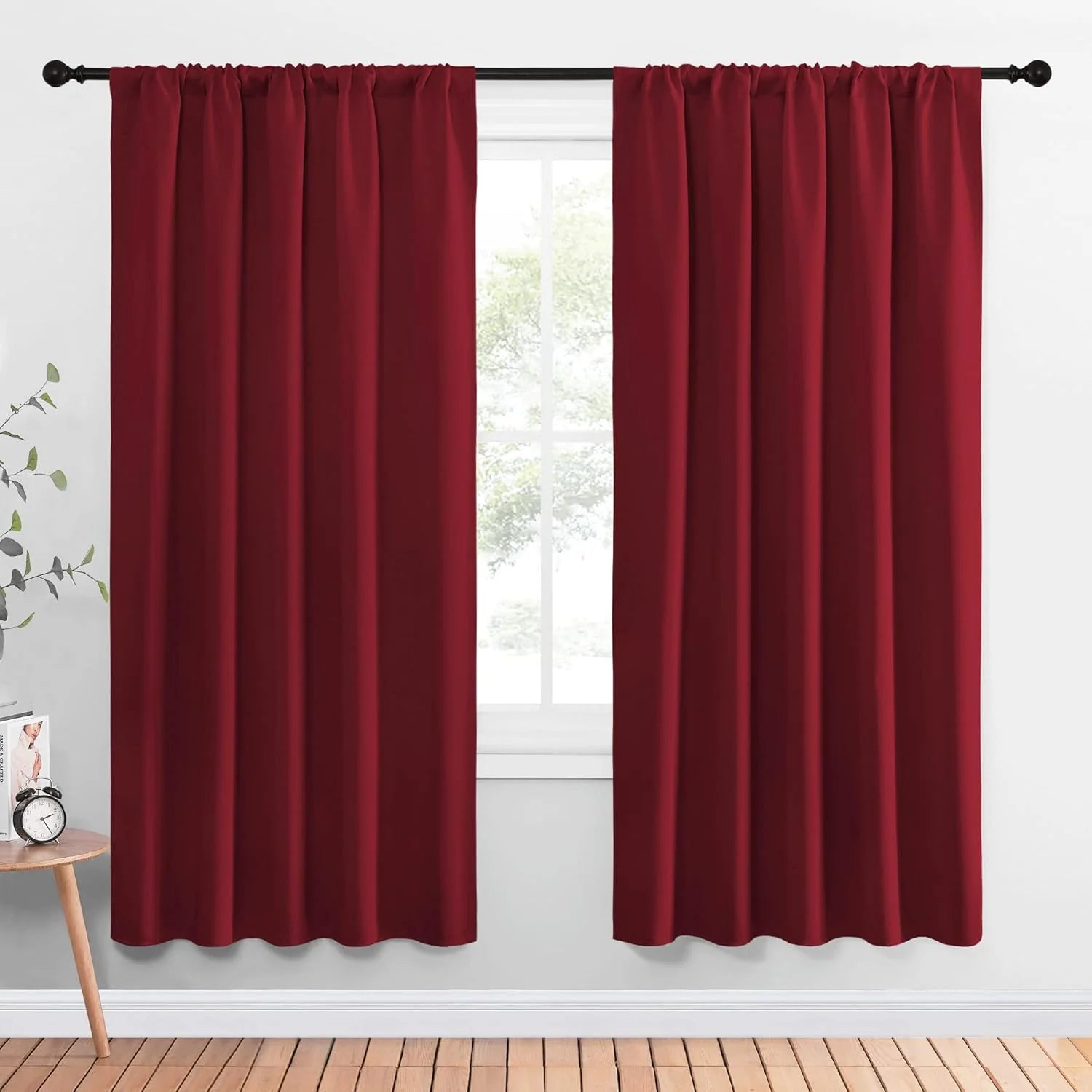 Burgundy rod pocket blackout curtains hanging on a black curtain rod by a bright window