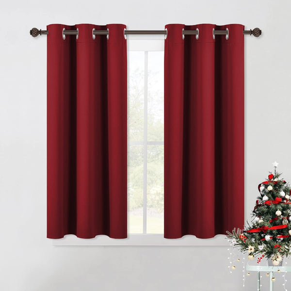 A pair of rich burgundy blackout curtains with silver grommets hangs on a bronze rod over a window.