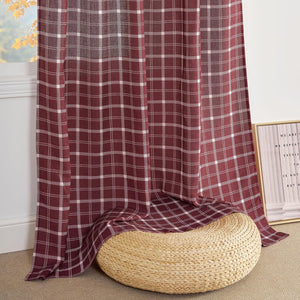 Burgundy and white plaid curtain panel hangs by a window, pooling on the floor next to a wicker pouf.