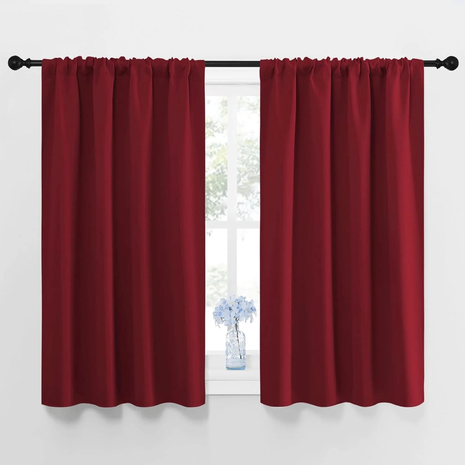 Deep red solid rod pocket curtains on black rod covering a bright window.
