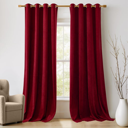 A pair of rich burgundy velvet grommet drapes hanging on a gold rod over a window in a bright room.