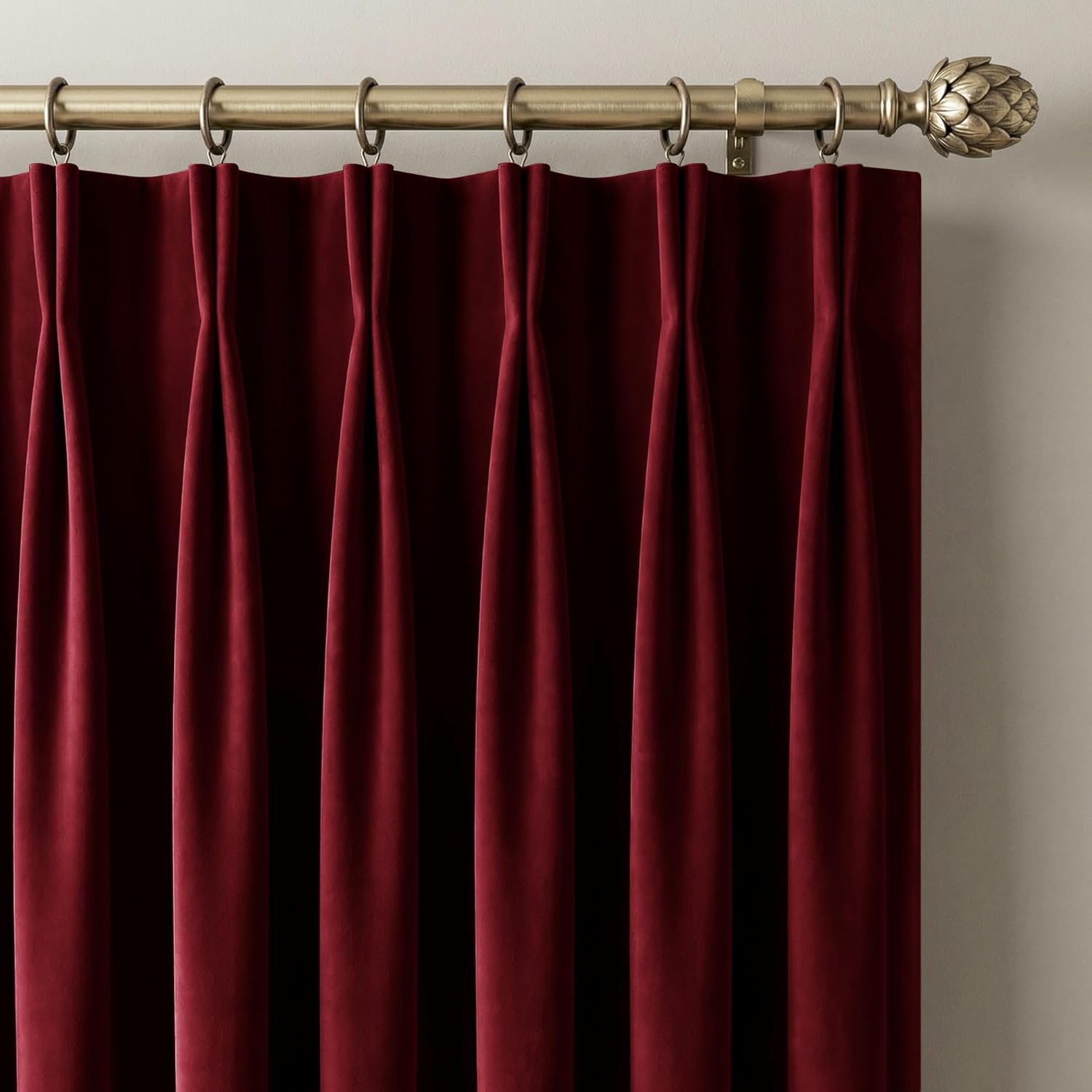 Burgundy velvet pinch pleat curtains hanging on a brass rod with ornate finial.