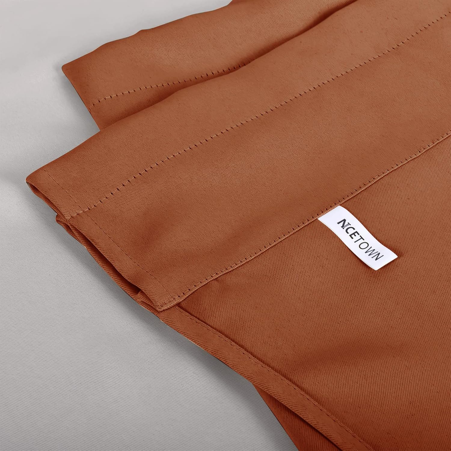 Close-up of burnt orange curtain panel. Shows matte woven fabric, stitched header, and NICETOWN brand label.