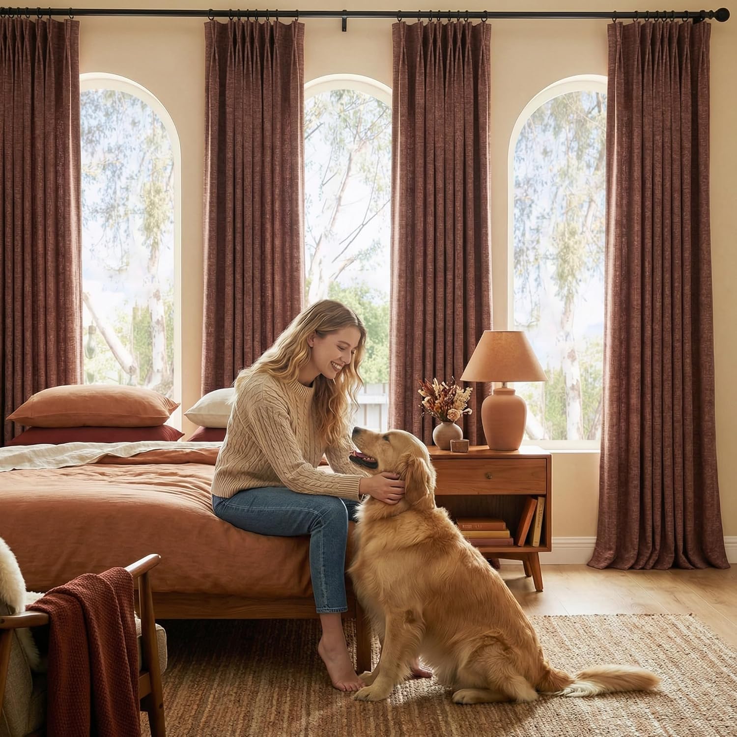 Burnt sienna textured pinch pleat curtains on a black rod framing arched windows in a warm bedroom.