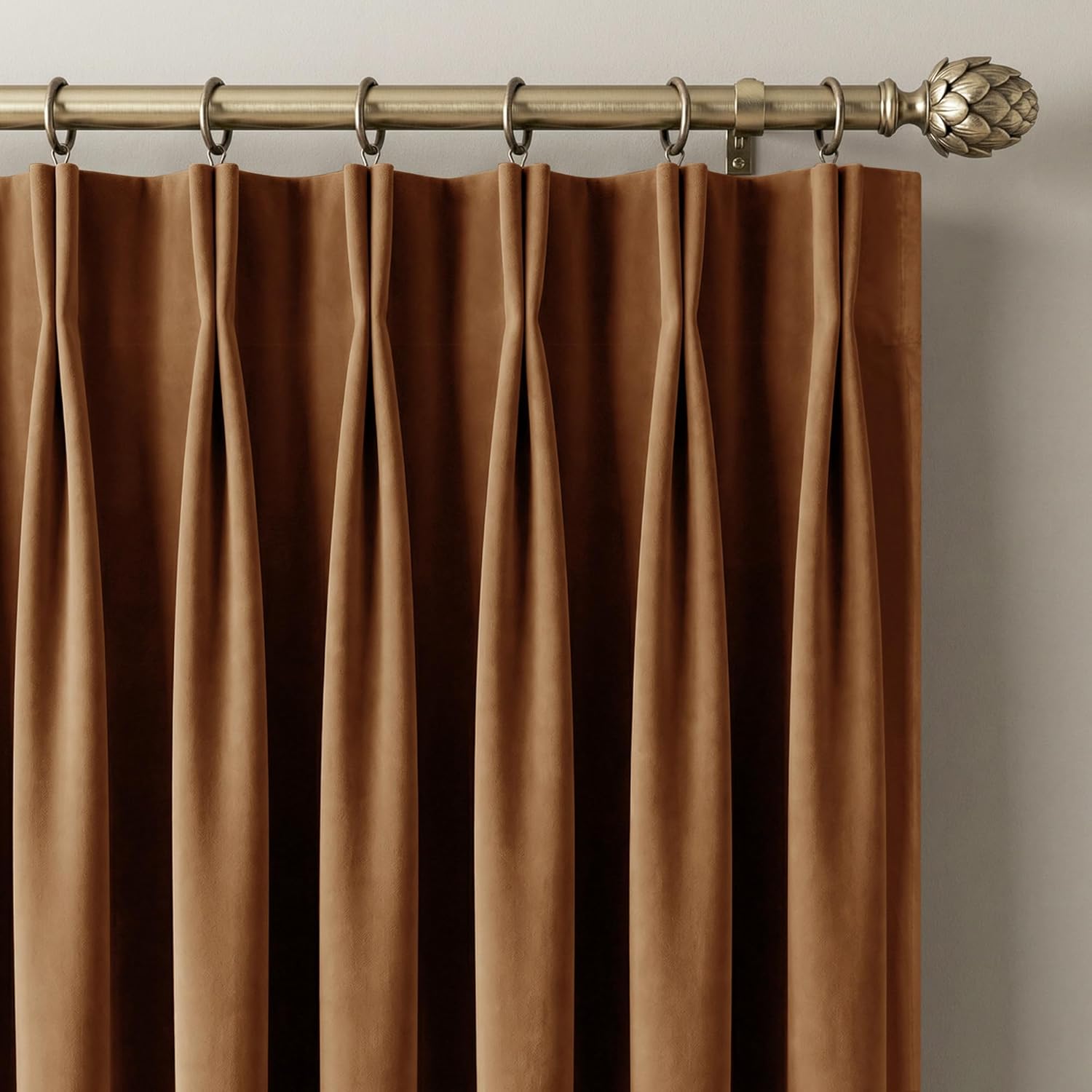 Camel brown velvet pinch pleat curtains hanging on an antique brass rod with a decorative finial.