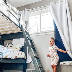 White grommet blackout curtains with dark blue liner next to a charcoal bunk bed with ladder.