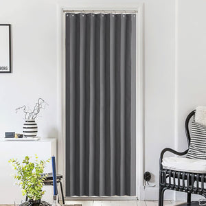 Charcoal gray blackout door curtain with silver grommets, hanging in a bright modern room.