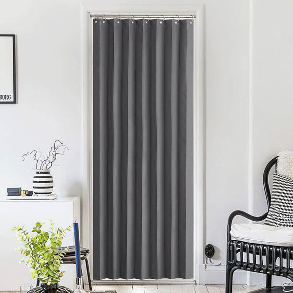 Charcoal gray blackout door curtain with silver grommets, hanging in a bright modern room.
