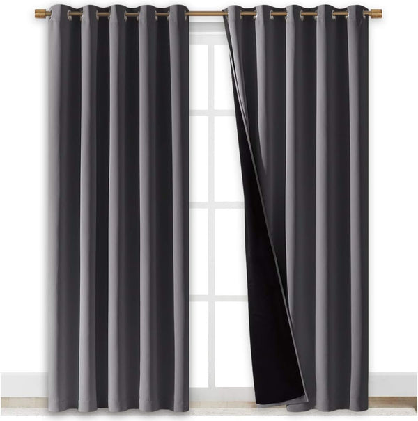 Charcoal gray blackout curtains with bronze grommet top hanging on a window. Black lining visible.