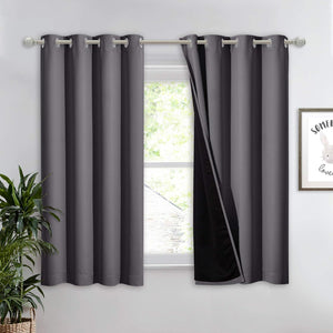 Pair of charcoal gray blackout curtains with silver grommets on a window rod, one pulled back to show black thermal lining.