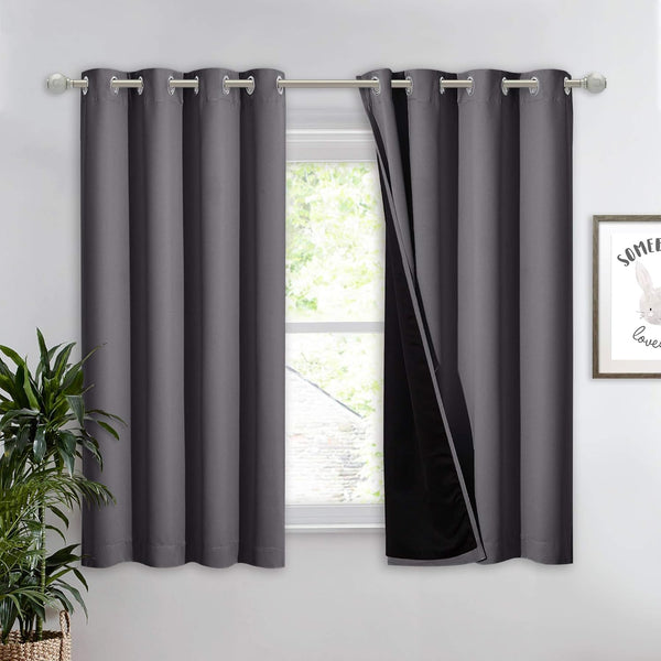 Pair of charcoal gray blackout curtains with silver grommets on a window rod, one pulled back to show black thermal lining.