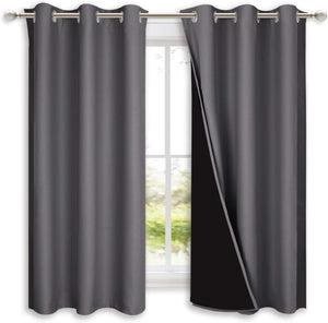 Charcoal grey grommet top blackout curtains, one revealing dark lining, on a silver rod.