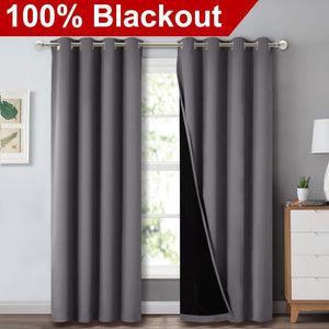 Charcoal grey blackout curtains with silver grommet tops on a window rod, revealing a thick black lining.