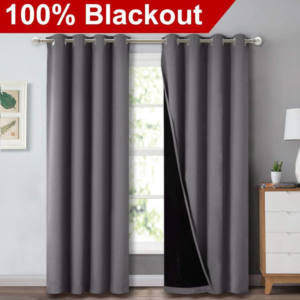 Charcoal grey blackout curtains with silver grommet tops on a window rod, revealing a thick black lining.