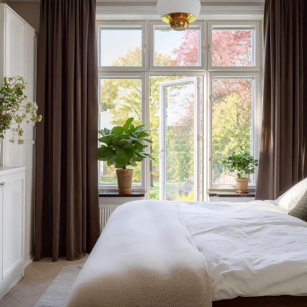 Thick chocolate brown full-length room darkening curtains hanging by a bright bedroom window.