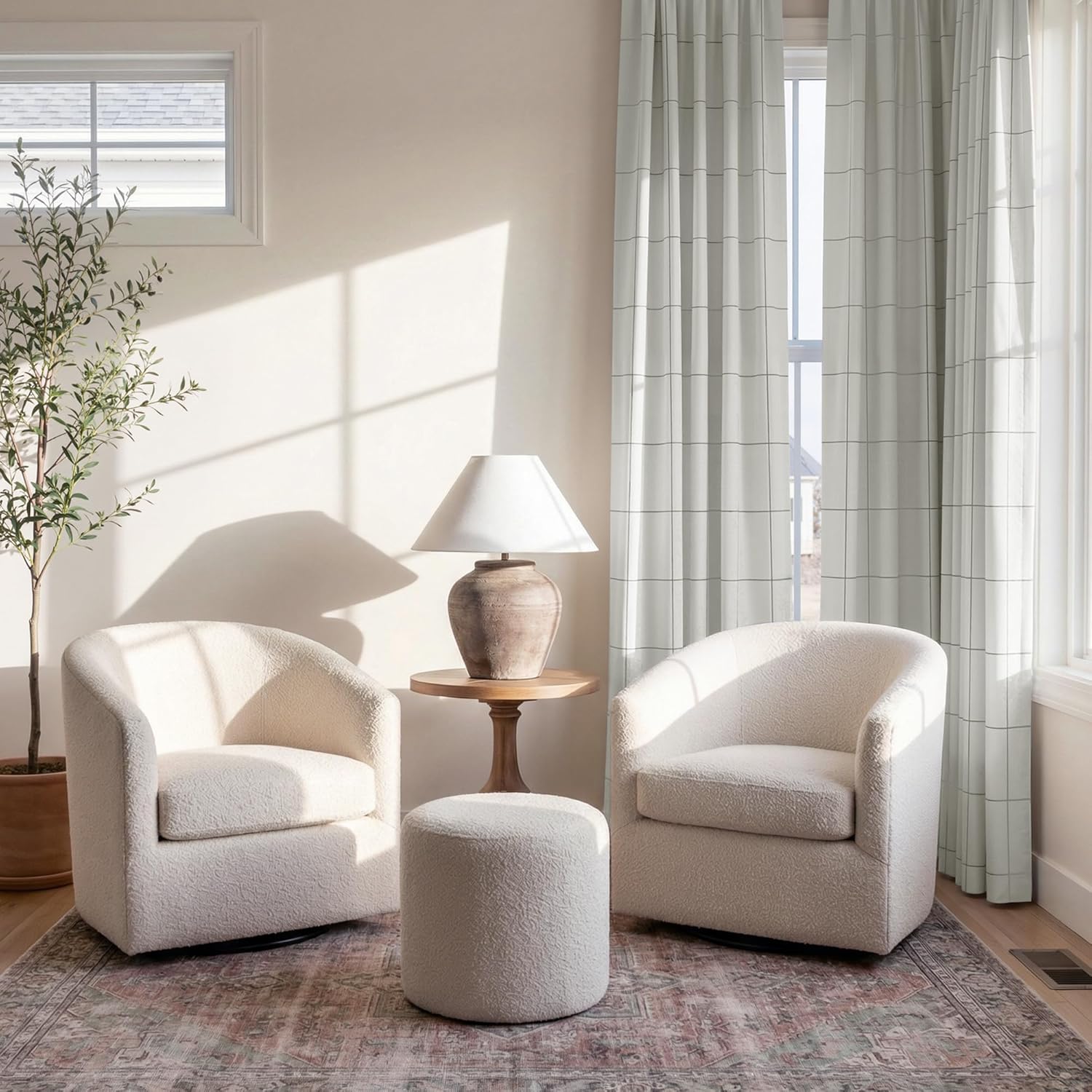 Two cream boucle barrel swivel chairs and matching round ottoman in a bright, modern living room.