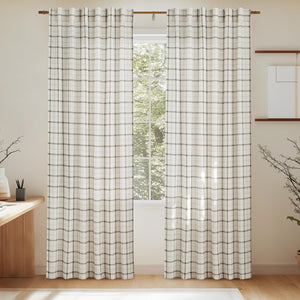 Two cream and brown plaid woven curtains softly filtering light, hanging on a wooden rod in a sunlit room.