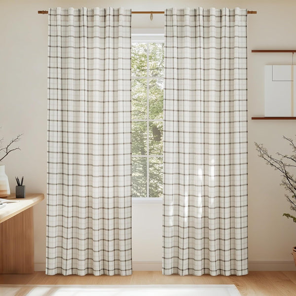 Two cream and brown plaid woven curtains softly filtering light, hanging on a wooden rod in a sunlit room.