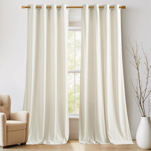 Pair of cream grommet top blackout curtains hanging on a wooden rod, pooling on the floor.