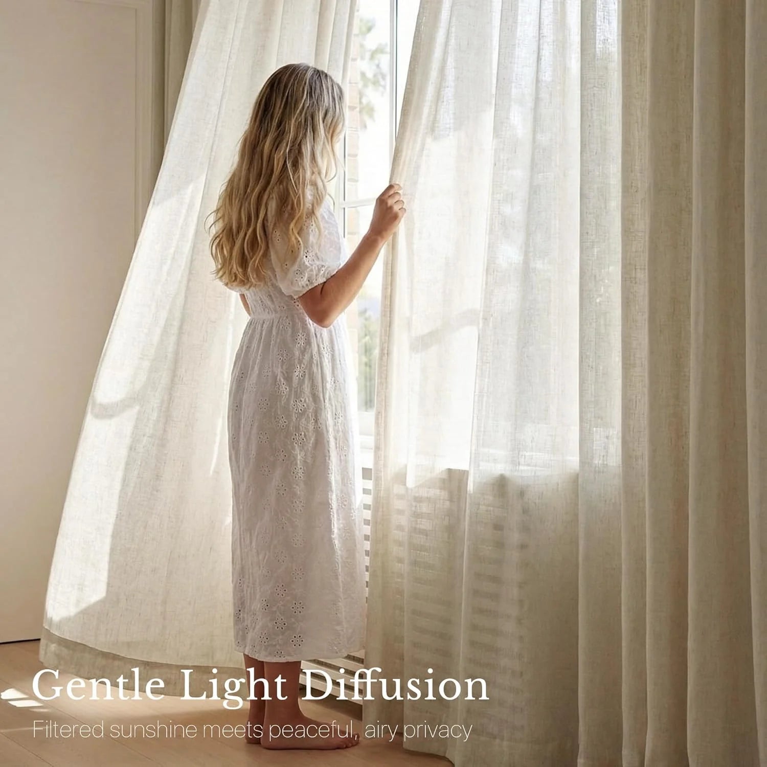 Blonde woman in white dress looking out window, holding back cream linen-look light-filtering curtains.