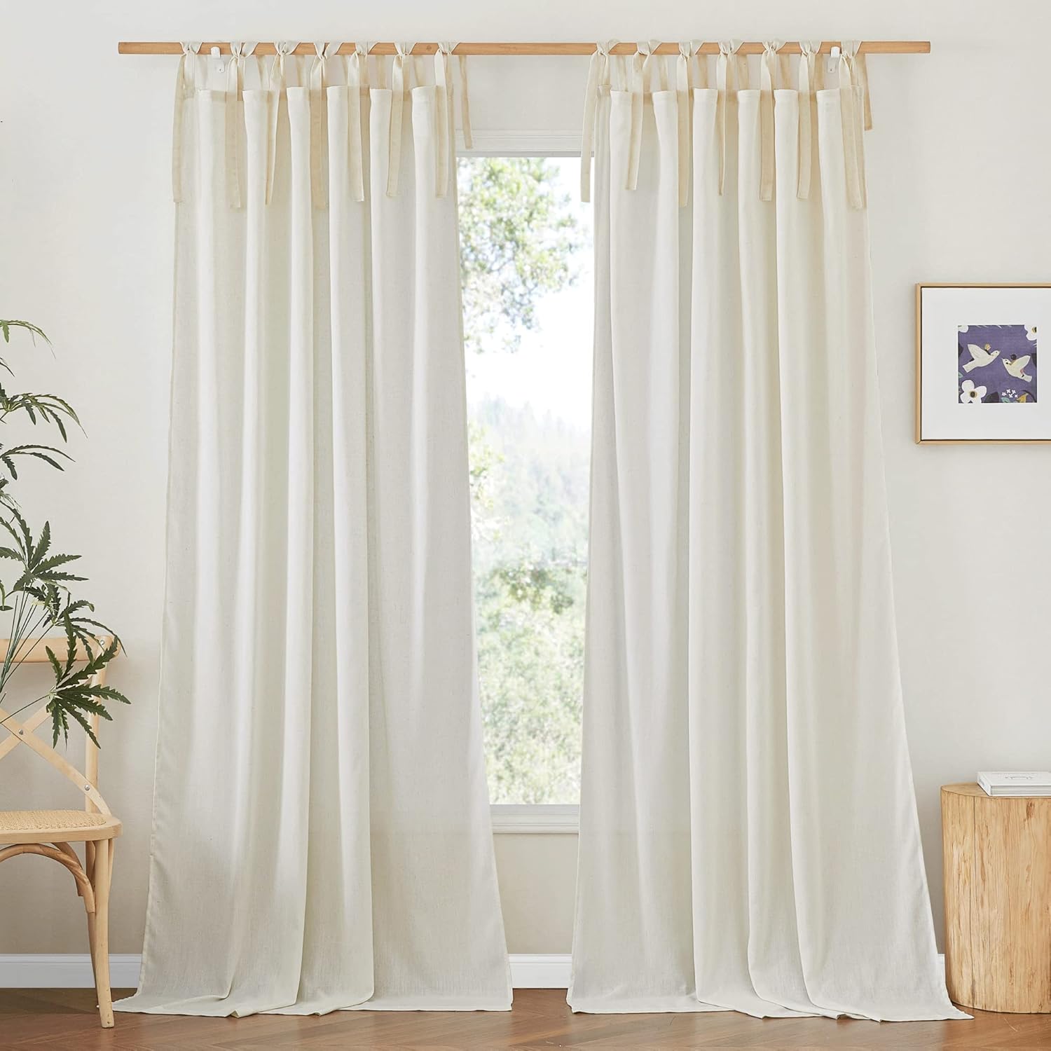 Creamy white linen tie-top curtains on a rustic wooden rod by a large window with greenery outside.