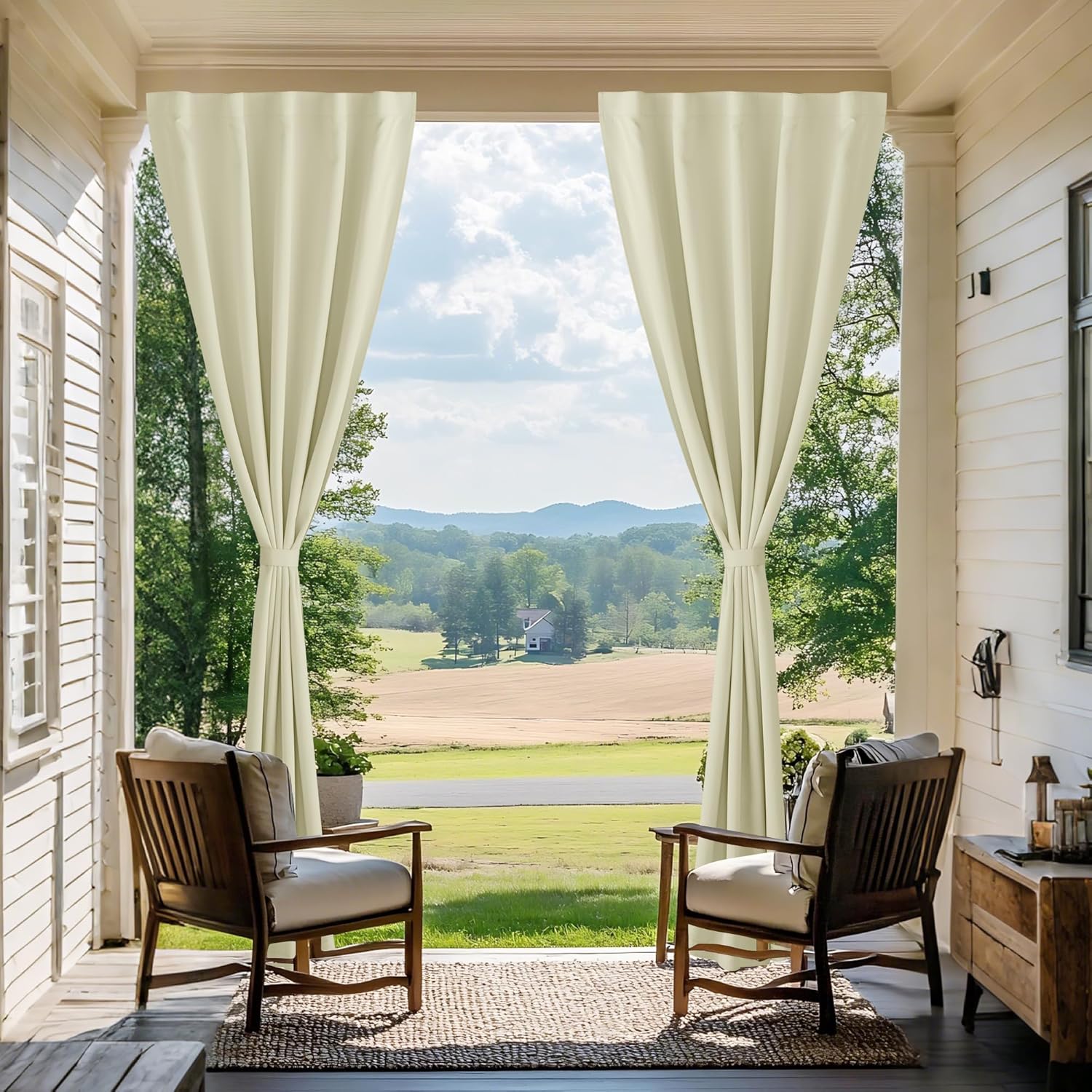 Pair of light cream outdoor porch curtains tied back, framing a scenic landscape view.