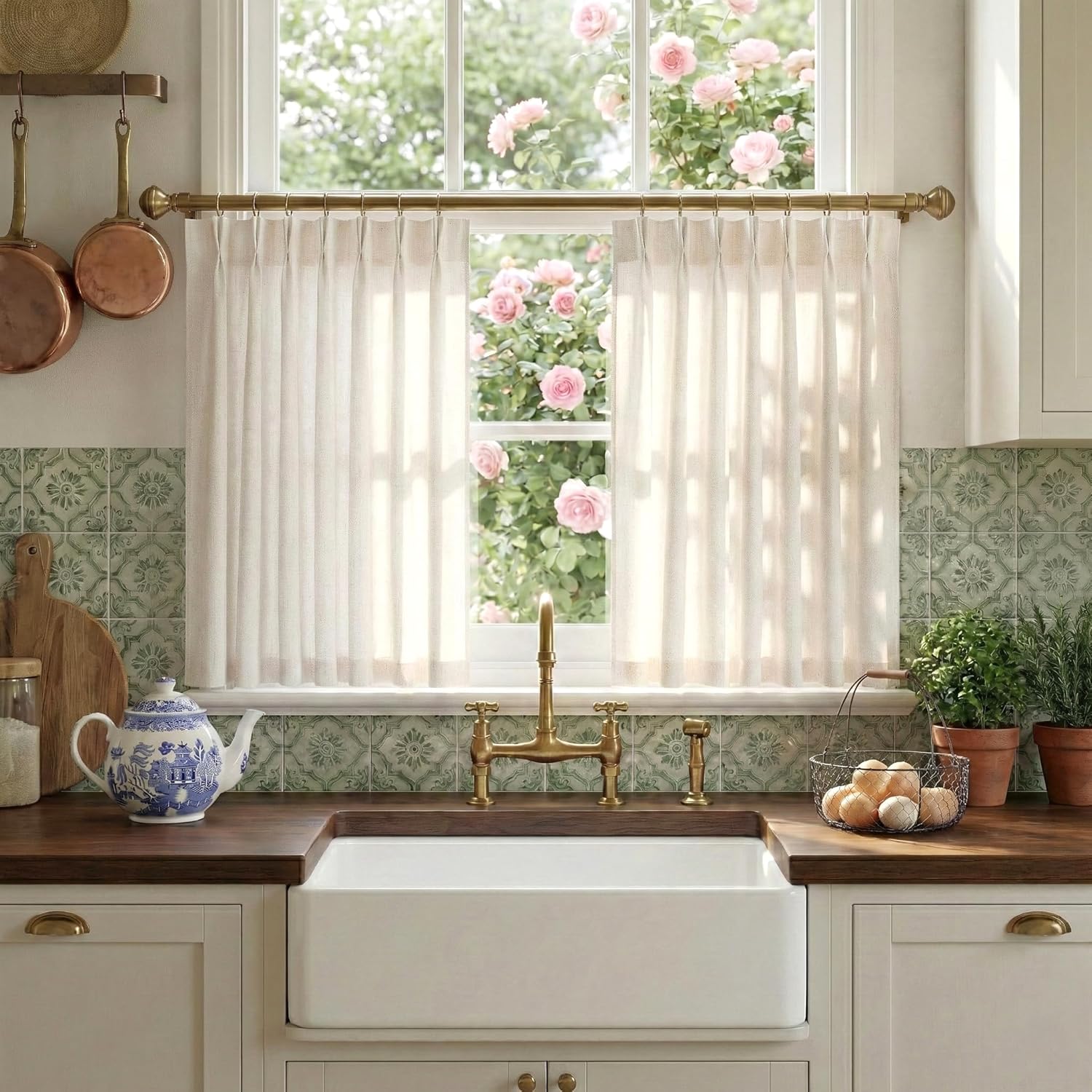Cream pleated sheer linen cafe curtains on a brass rod in a sunny kitchen over a farmhouse sink.