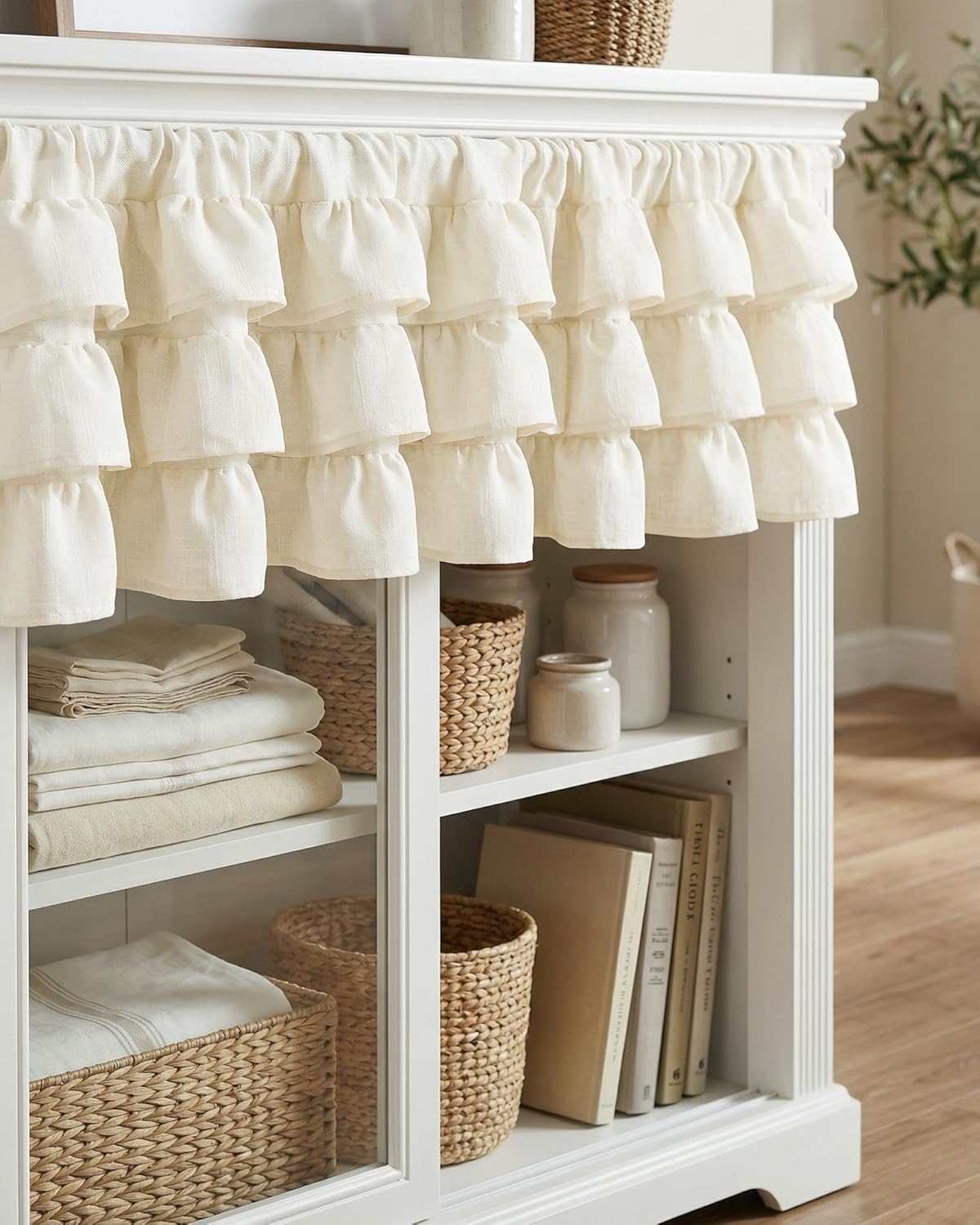 Cream, multi-tiered ruffled linen valance with a rod pocket, adorning a white cabinet.