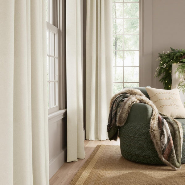 Cream textured full-length drapes hanging elegantly by a large window in a cozy, naturally lit living room.