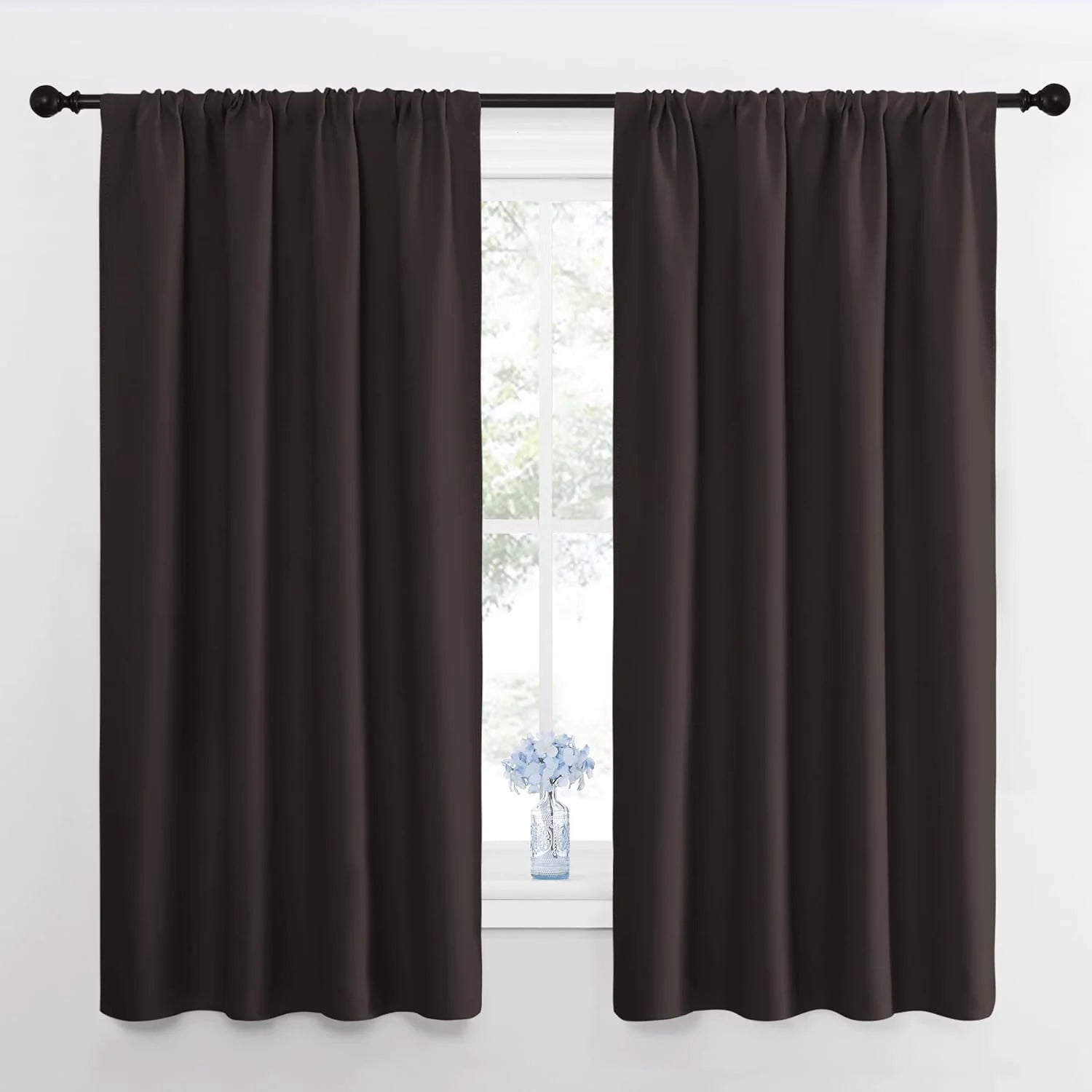 Dark brown rod pocket blackout curtains hanging on a black rod over a window with a small blue vase.