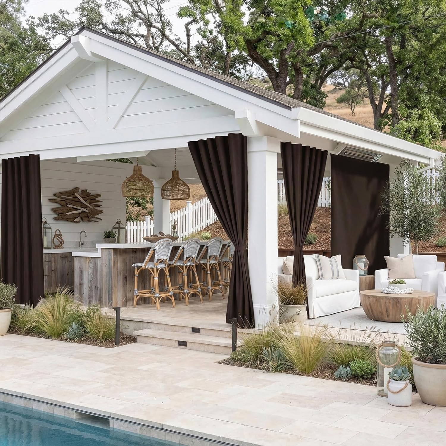 Dark brown outdoor privacy curtains hanging on a white poolside cabana with a bar and lounge seating.