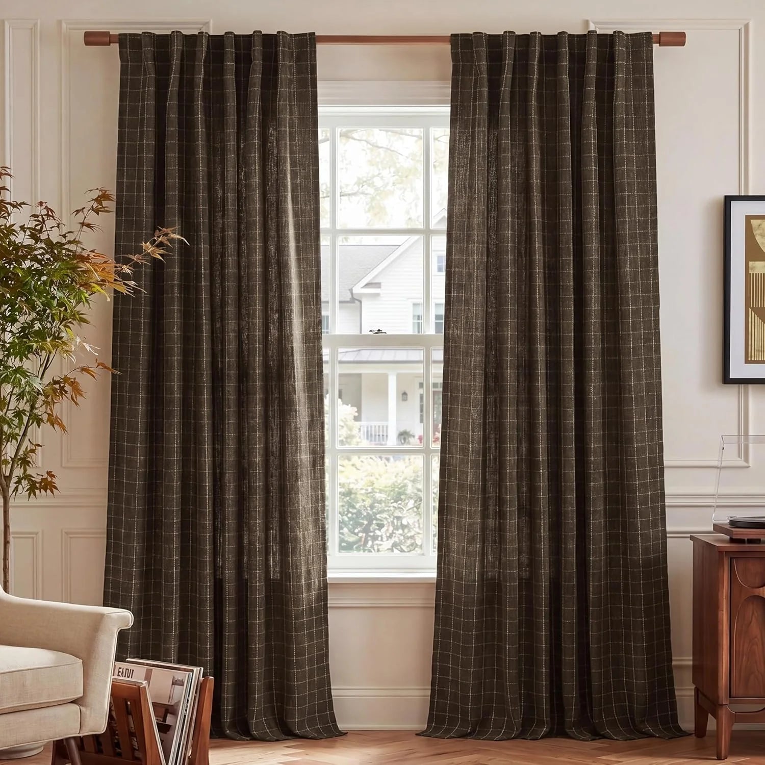 Pair of dark brown windowpane pleated curtains on a wooden rod in a bright living room with wooden floors.