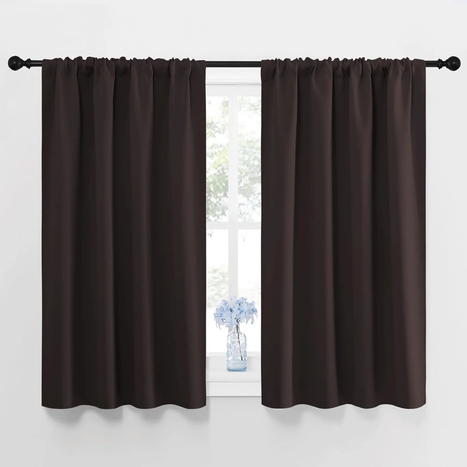 Dark brown rod pocket curtains hanging on a black curtain rod over a bright window