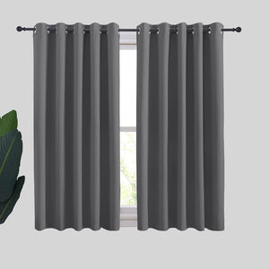 Two dark gray blackout curtain panels with silver grommet tops hang on a black rod above a window.