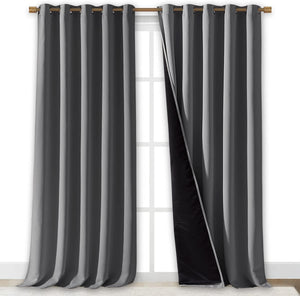 Pair of dark gray blackout curtains with bronze grommet tops on a rod. One panel is open, showing the black lining.