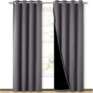 Pair of dark gray blackout grommet curtains on a silver rod, one pulled back to show black lining, covering a window.