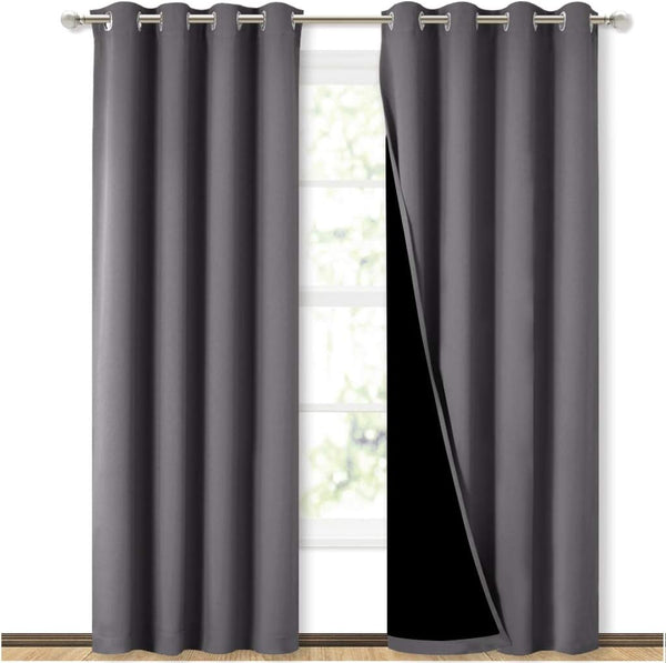 Pair of dark gray blackout grommet curtains on a silver rod, one pulled back to show black lining, covering a window.