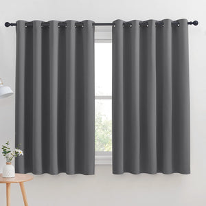 Pair of dark gray blackout curtains with black grommet tops hanging on a black rod over a window.