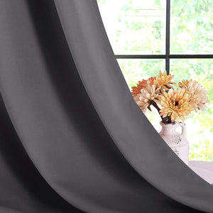 Close-up of dark gray blackout curtain panel draped softly by a window, with a vase of orange flowers visible.