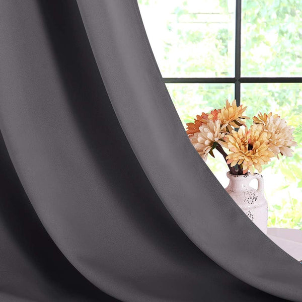 Close-up of dark gray blackout curtain panel draped softly by a window, with a vase of orange flowers visible.
